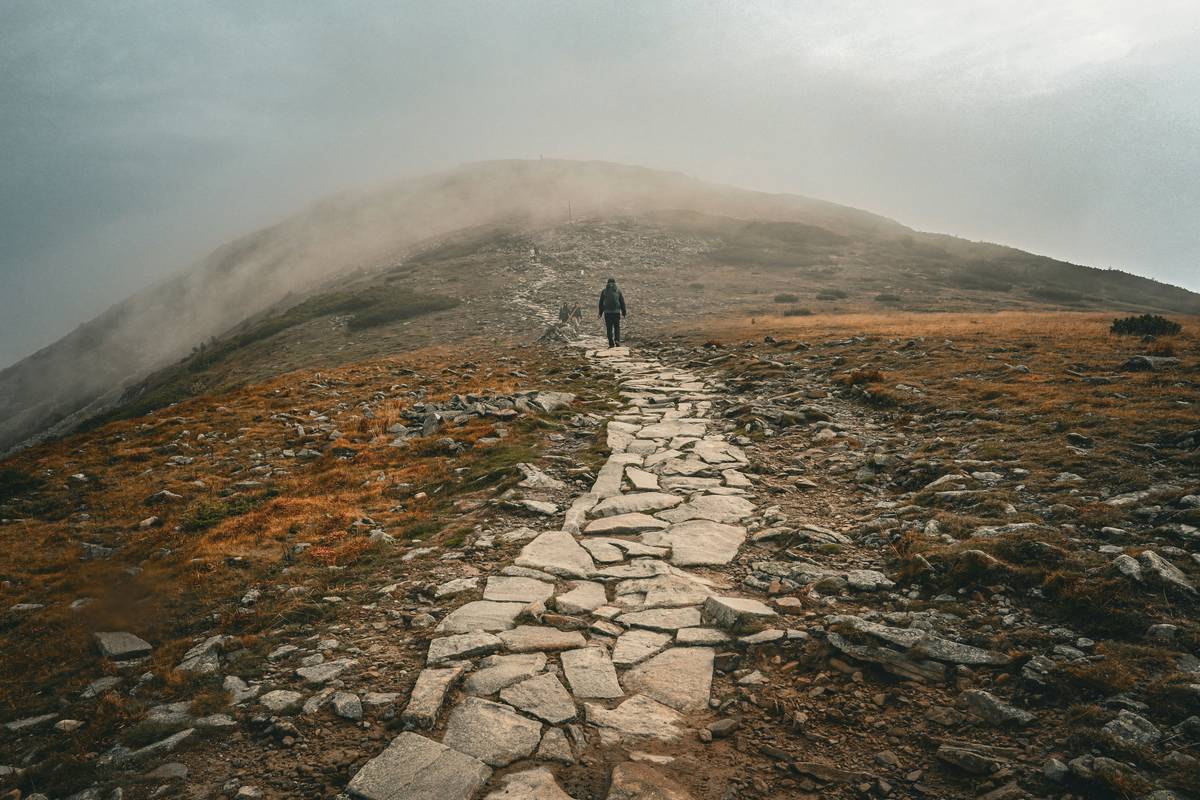 A woman wearing hiking gear stands at a mountain summit during sunrise