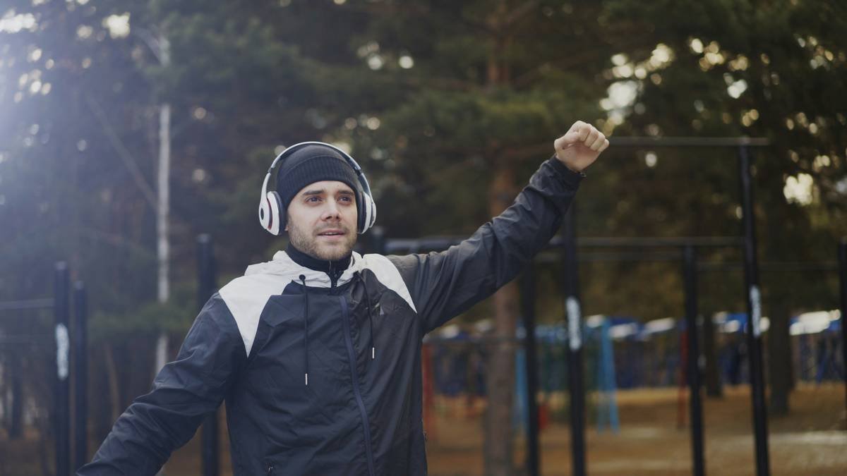 Handsome man in headphones doing stretching exercise while listening music in winter park outdoors
