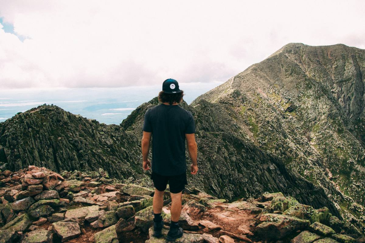 A man stands on a rocky mountain ridge overlooking peaks.