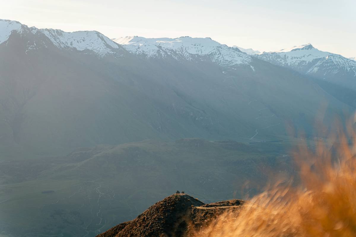 Snow-capped mountains under a hazy sky with dry grass.