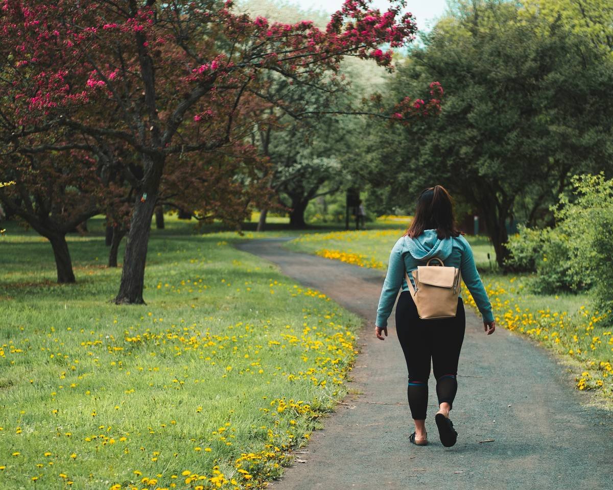 woman wearing blue jacket and black pants walking on grass field pathway
